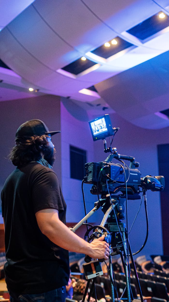 A videographer operates a camera capturing a large event indoors.